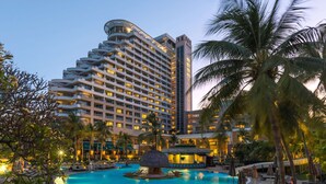 Un hotel con una amplia piscina rodeada de palmeras y sillones de descanso.