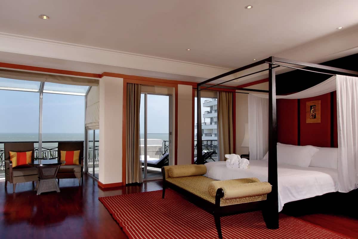 Een ruime slaapkamer met een hemelbed, een balkon met uitzicht op zee en een zithoek met een tafel en stoelen.