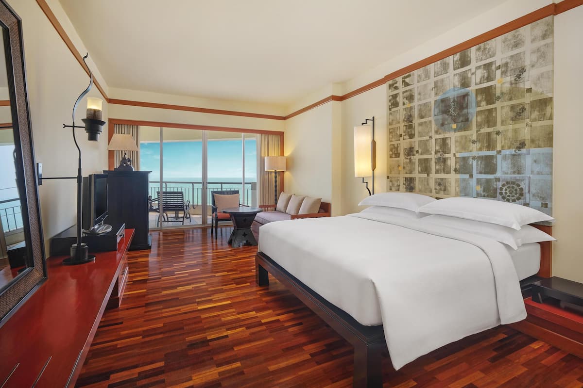 Een hotelkamer met een groot bed, een bureau, een stoel en uitzicht op de oceaan.