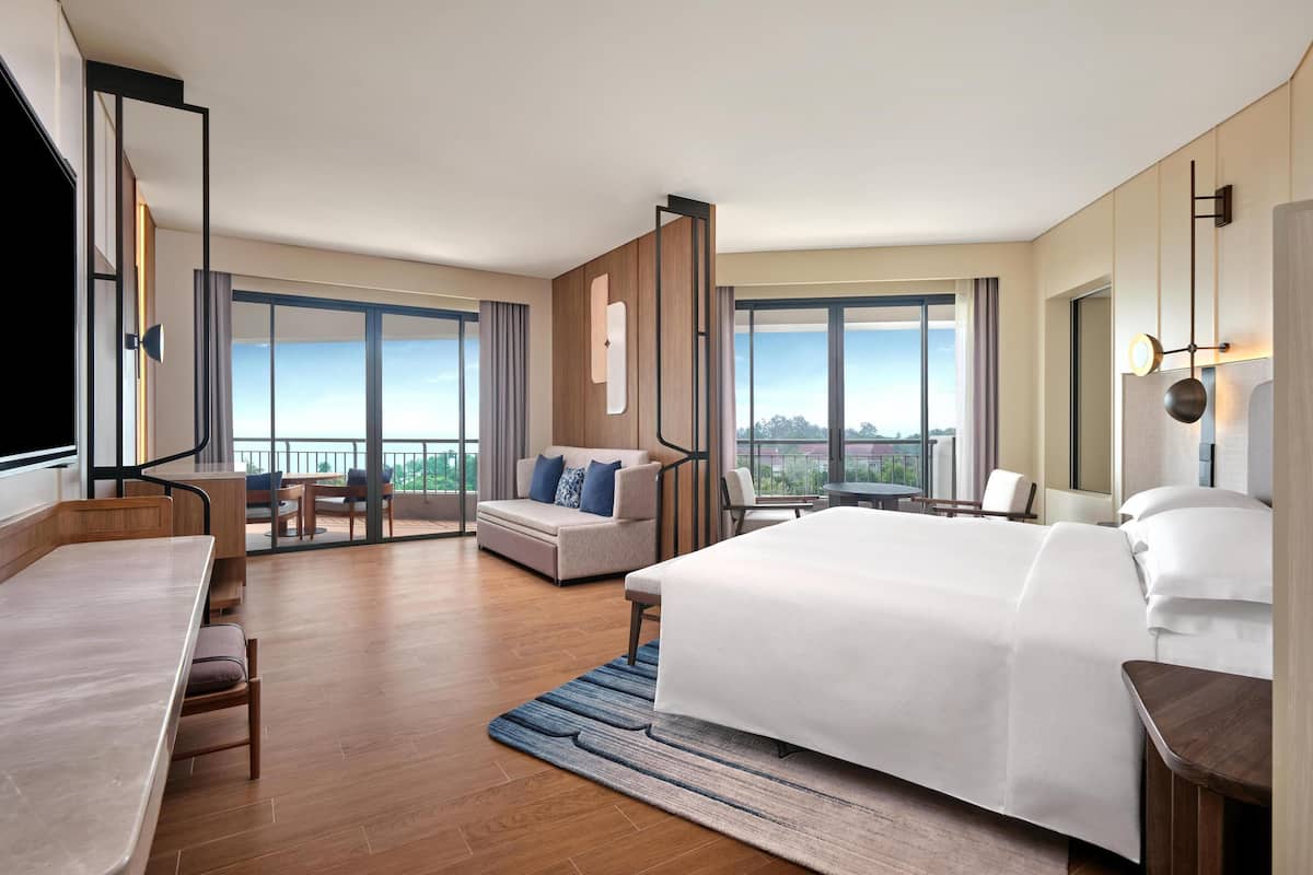 Een moderne hotelkamer met een groot bed, een bureau, een bank en een balkon met uitzicht.