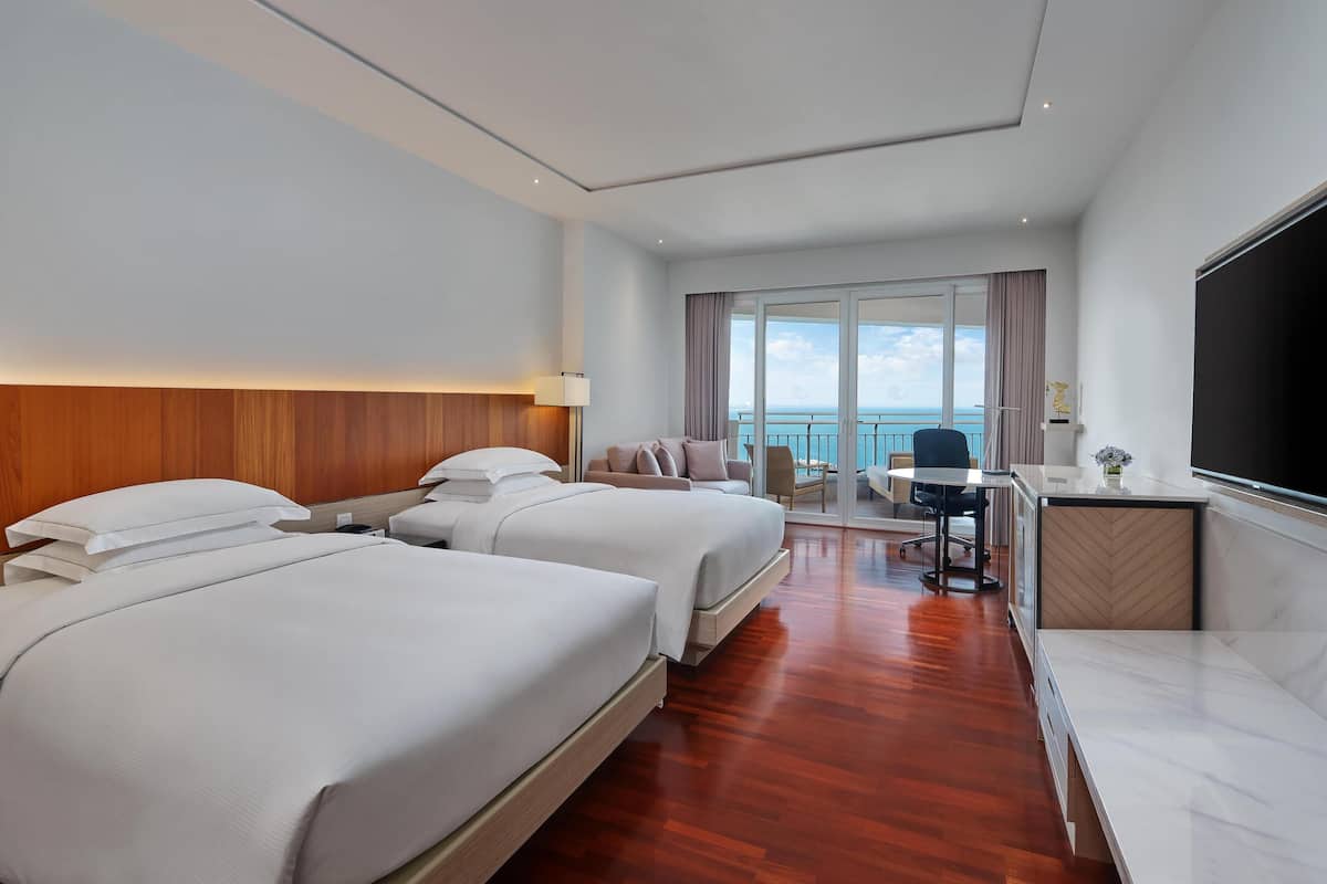 Een hotelkamer met twee bedden, een bureau, een stoel en uitzicht op zee.