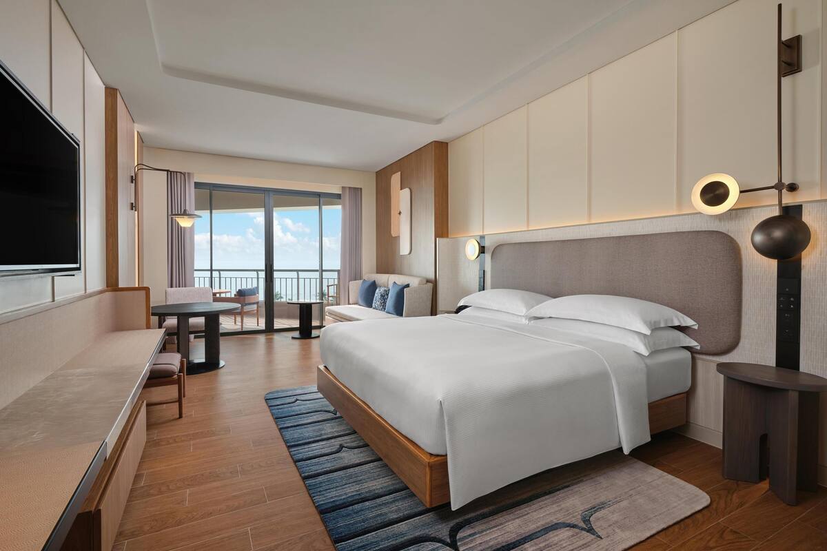 Een moderne hotelkamer met een groot bed, een bureau, een stoel en een balkon met uitzicht.