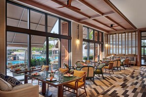 Un vaste espace intérieur aménagé en salle à manger, doté de grandes fenêtres, de poutres en bois au plafond et d’un sol à carreaux.