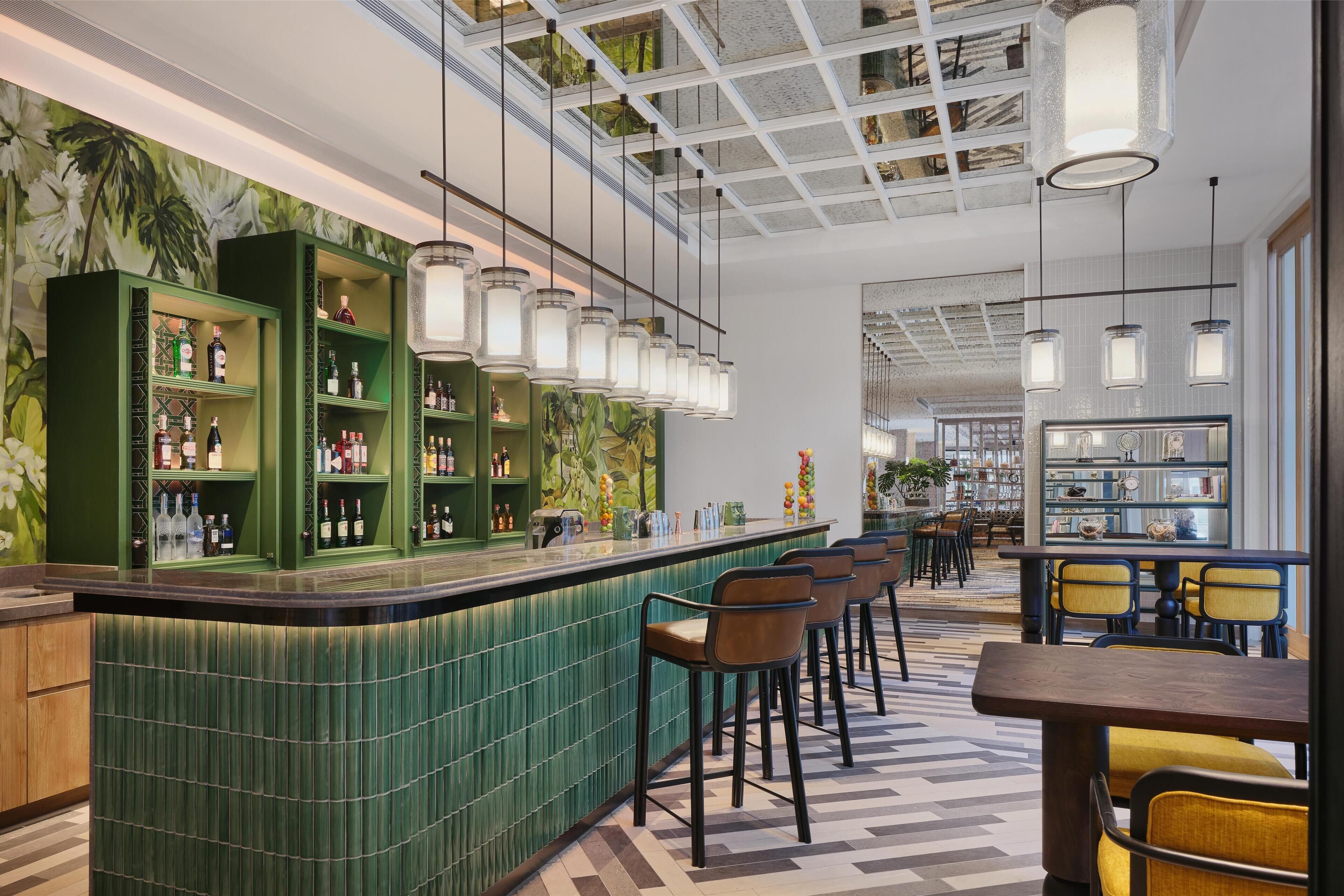 A bar area with green shelving, bar stools, and hanging pendant lights.