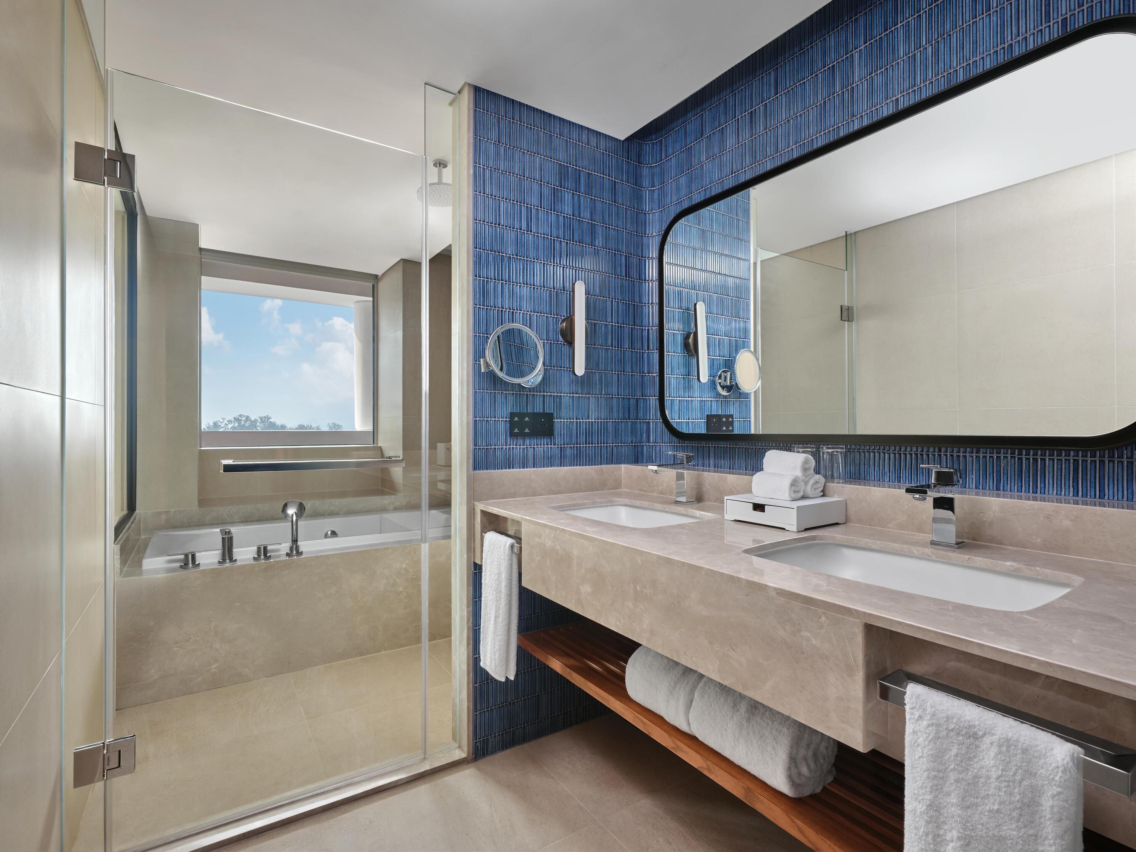 A modern bathroom with two sinks, a large mirror, and a glass-enclosed shower.