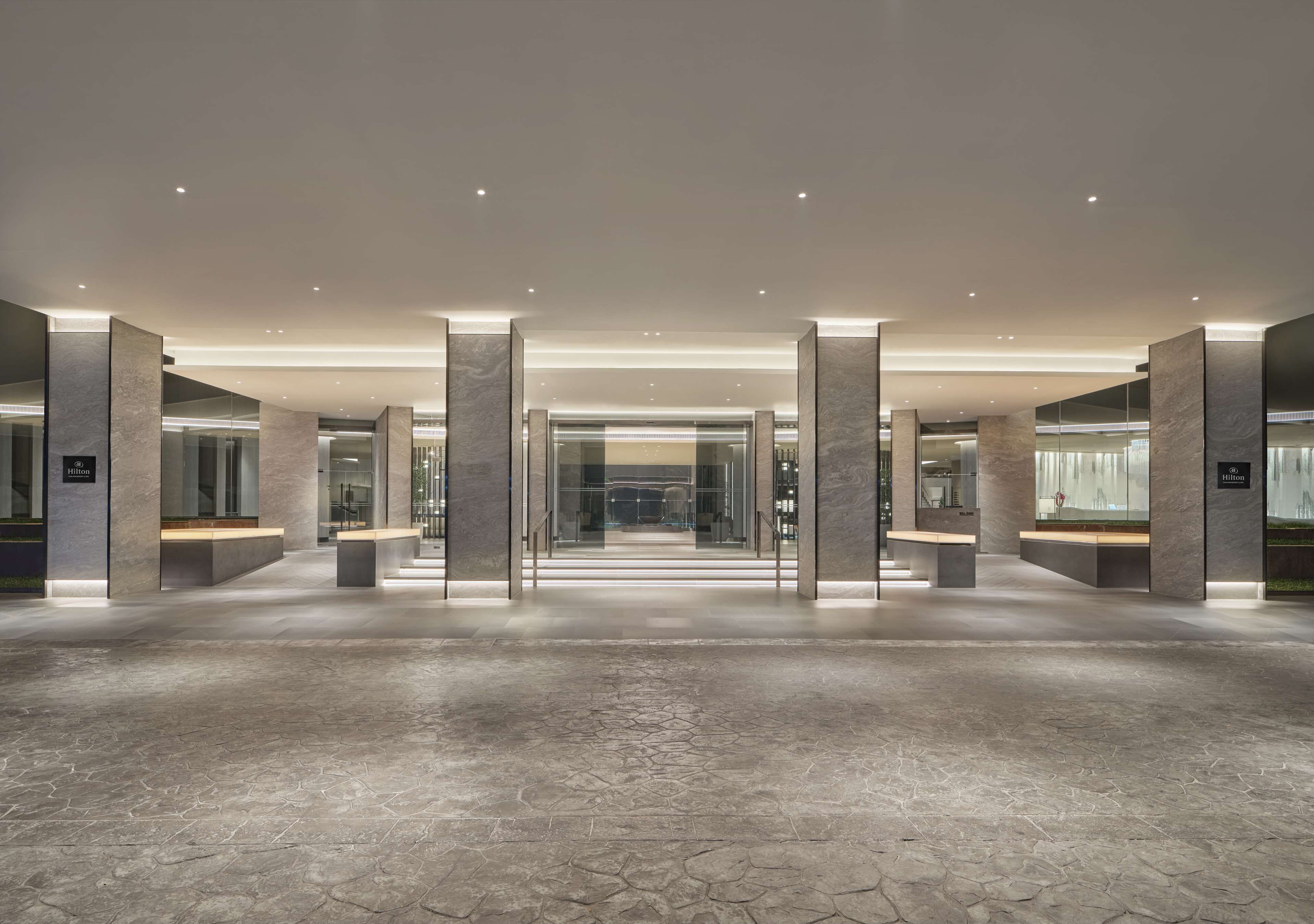 A spacious lobby with a modern design, featuring a central open area, seating arrangements, and a visible reception desk.