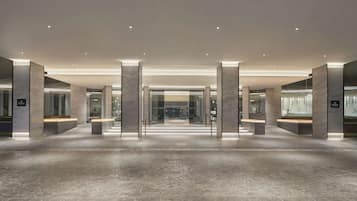 A spacious lobby with a modern design, featuring a central open area, seating arrangements, and a visible reception desk.