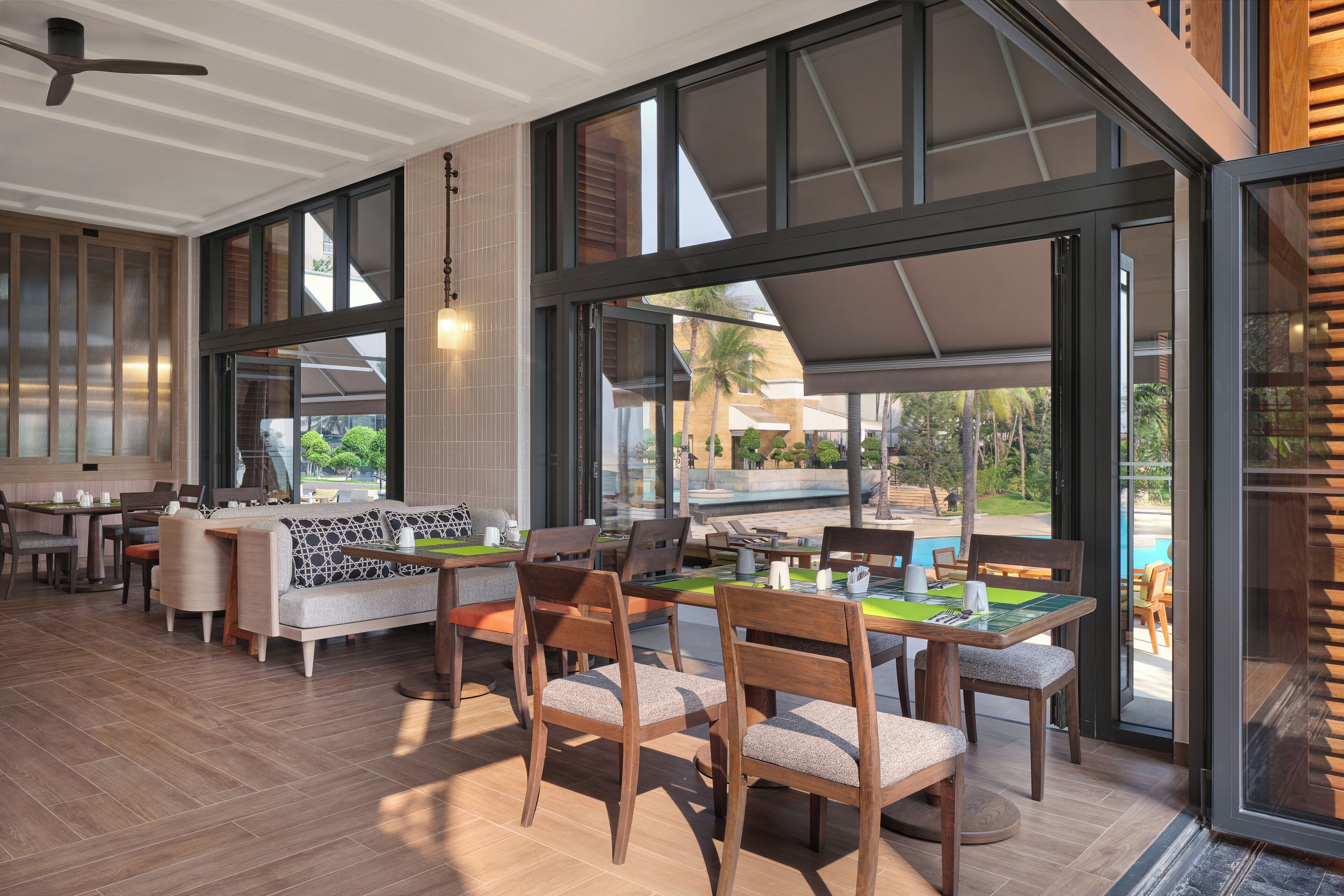 An indoor dining area with wooden furniture, large windows, and a view of the outdoor pool.