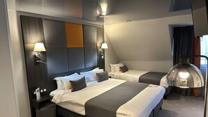 Habitación de hotel con dos camas, cabecero oscuro, lámparas fijadas a la pared y un espejo grande.