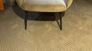 Una silla de diseño original con forma de volutas, ubicada en una habitación con piso alfombrado y una ventana con cortinas.