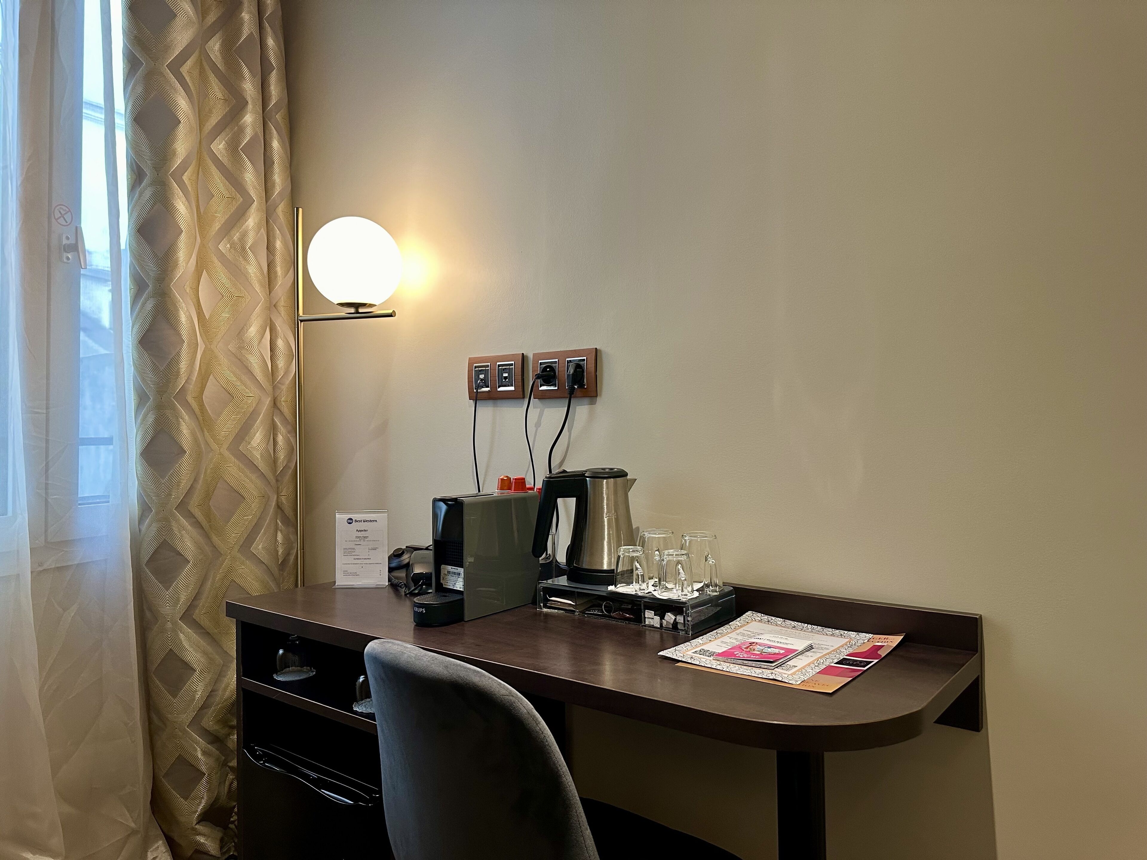 A hotel room with a desk, a lamp, a coffee machine, and a sign indicating the room type.