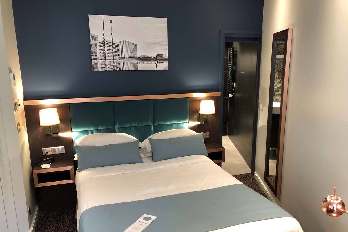 Hotelkamer met een groot bed, twee nachtkastjes met lampen, een hoofdbord, een aan de muur hangend schilderij en een deur.