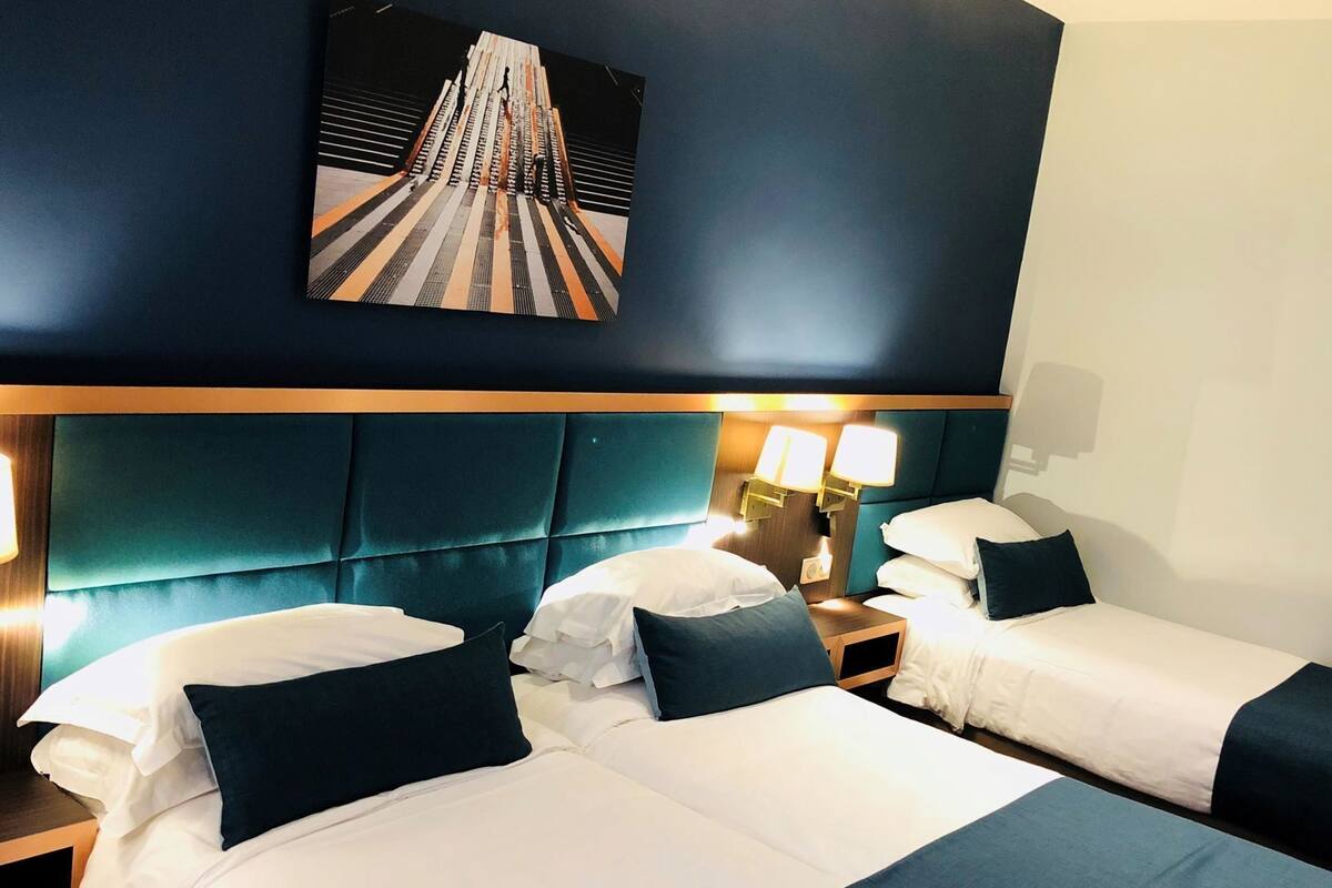 Een hotelkamer met twee bedden, een hoofdeinde, nachtlampjes en een schilderij aan de muur.