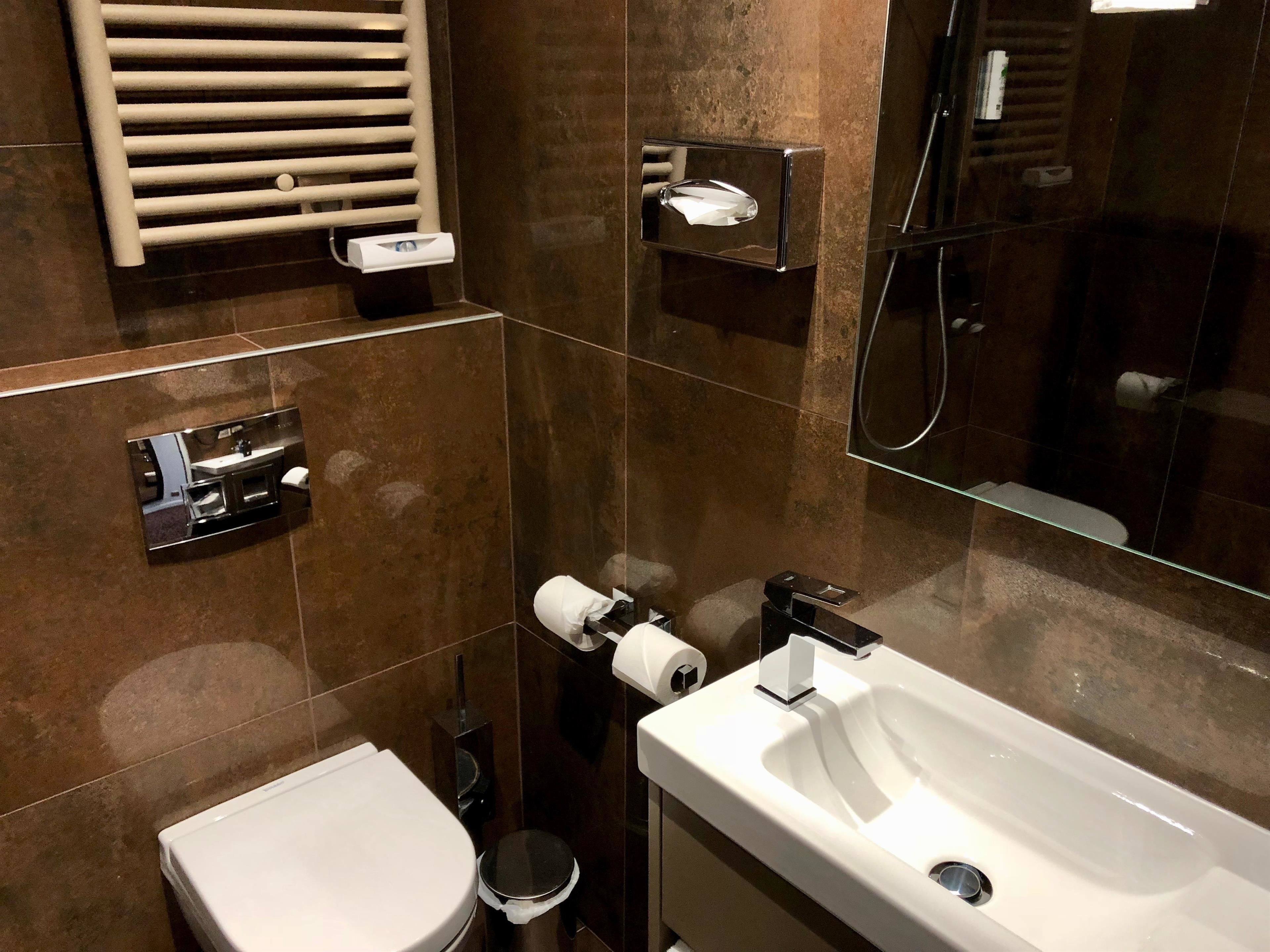 Une salle de bain moderne avec un lavabo, des toilettes et un bidet, tous de couleur blanche. On y trouve également un porte-serviettes, un miroir et une cabine de douche en verre.