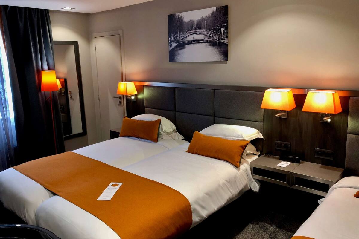 Hotelkamer met twee bedden, een hoofdeinde, nachtlampjes, een nachtkastje, een aan de muur hangend schilderij en een deur.