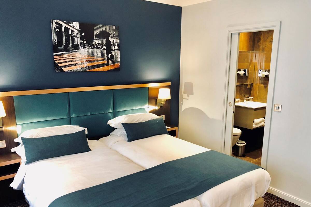 Een hotelkamer met een bed, nachtkastjes, een wandlamp en een deur naar de badkamer.