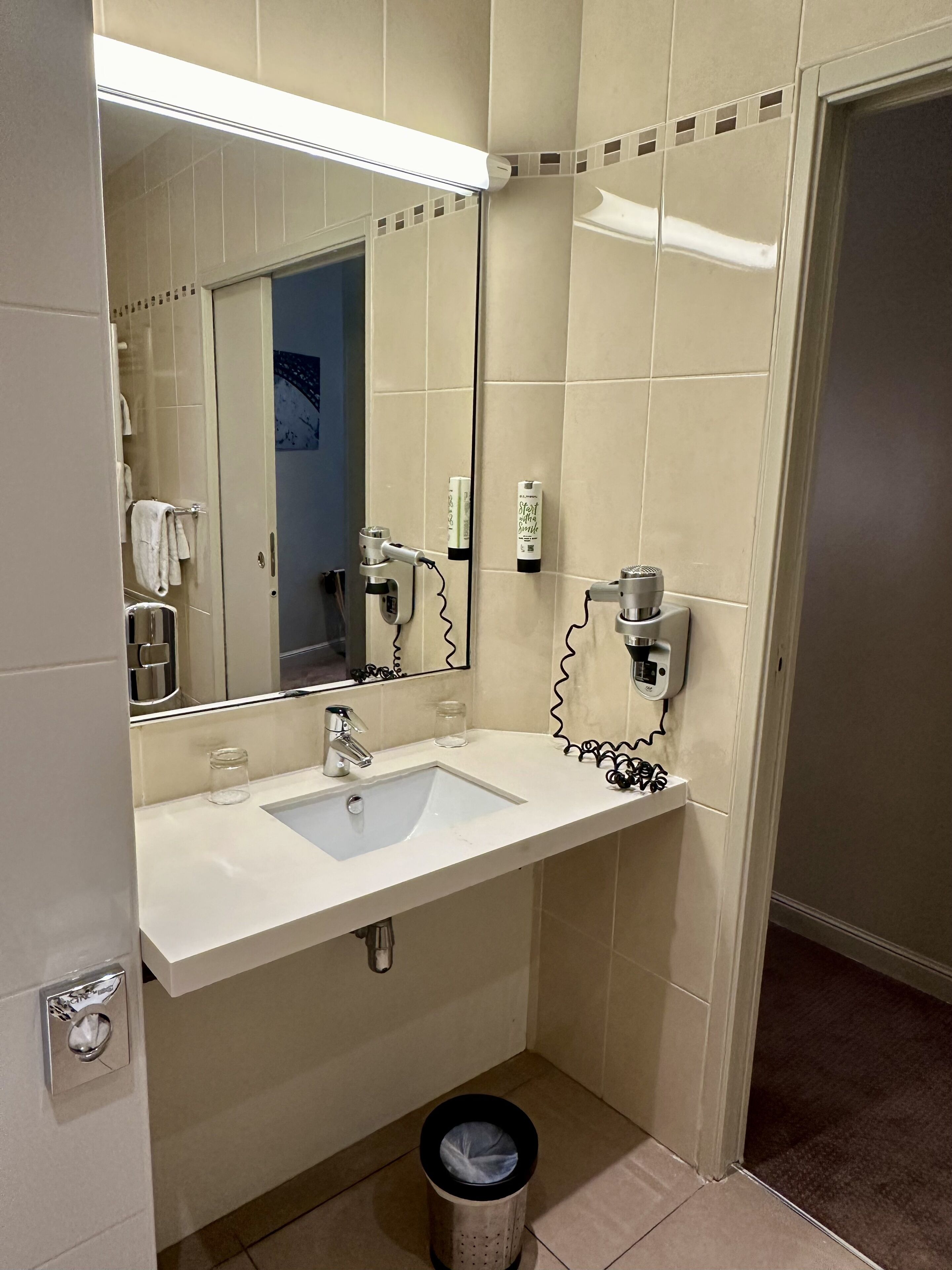 A bathroom with a white sink, a mirror, a towel rack, and a trash can.