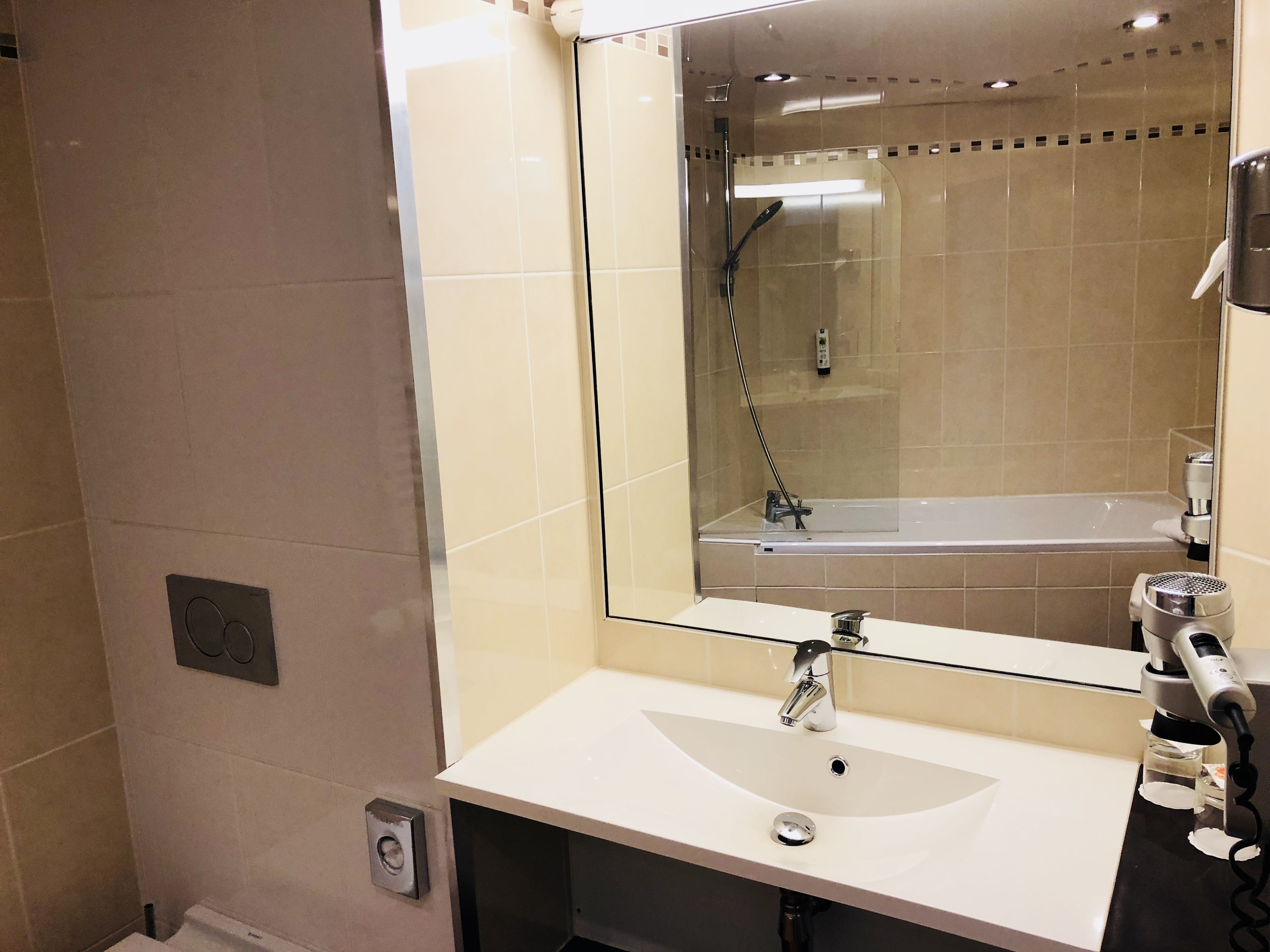 Un baño moderno con ducha envuelta en vidrio, un lavabo blanco y un secador de pelo en la encimera.