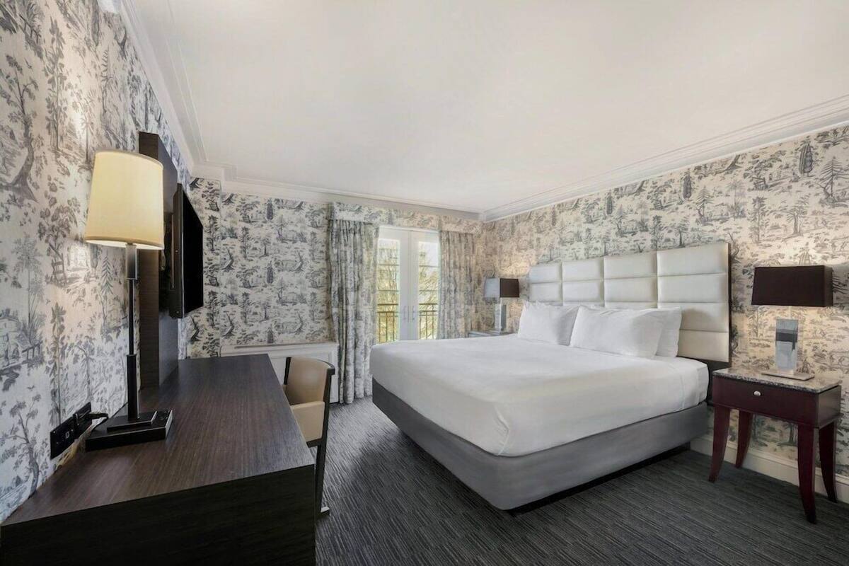 A hotel room with a large bed, a desk, a chair, a TV, and a window with curtains.