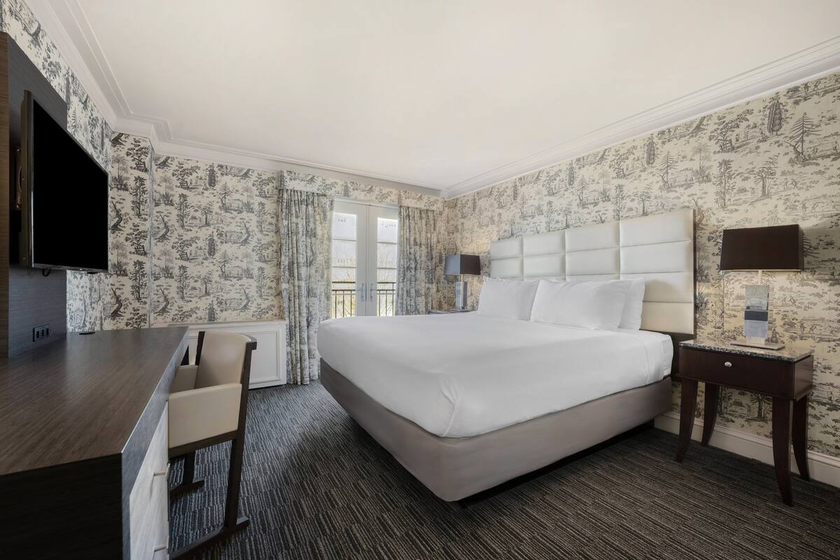 A hotel room with a large bed, a desk with a chair, a TV, and a window with curtains.