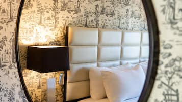 A bedroom with a headboard, a bedside lamp, and patterned wallpaper.