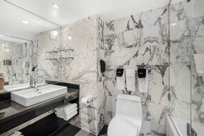 Features a sleek sink, white vanity, and marble walls with a glass shelf for toiletries.