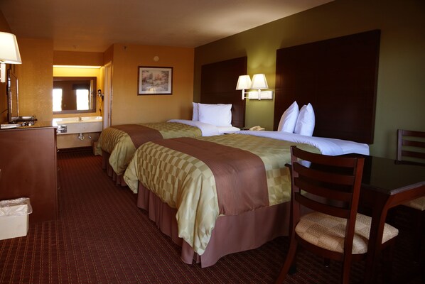 A hotel room with two beds, a desk, a chair, a desk lamp, a telephone, and a mirror.