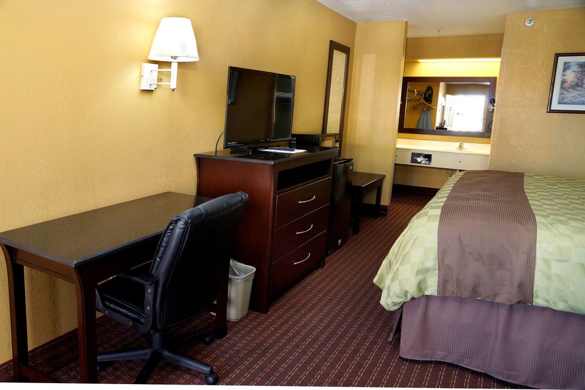 Una habitación de hotel con escritorio, silla, cama, cómoda y espejo.