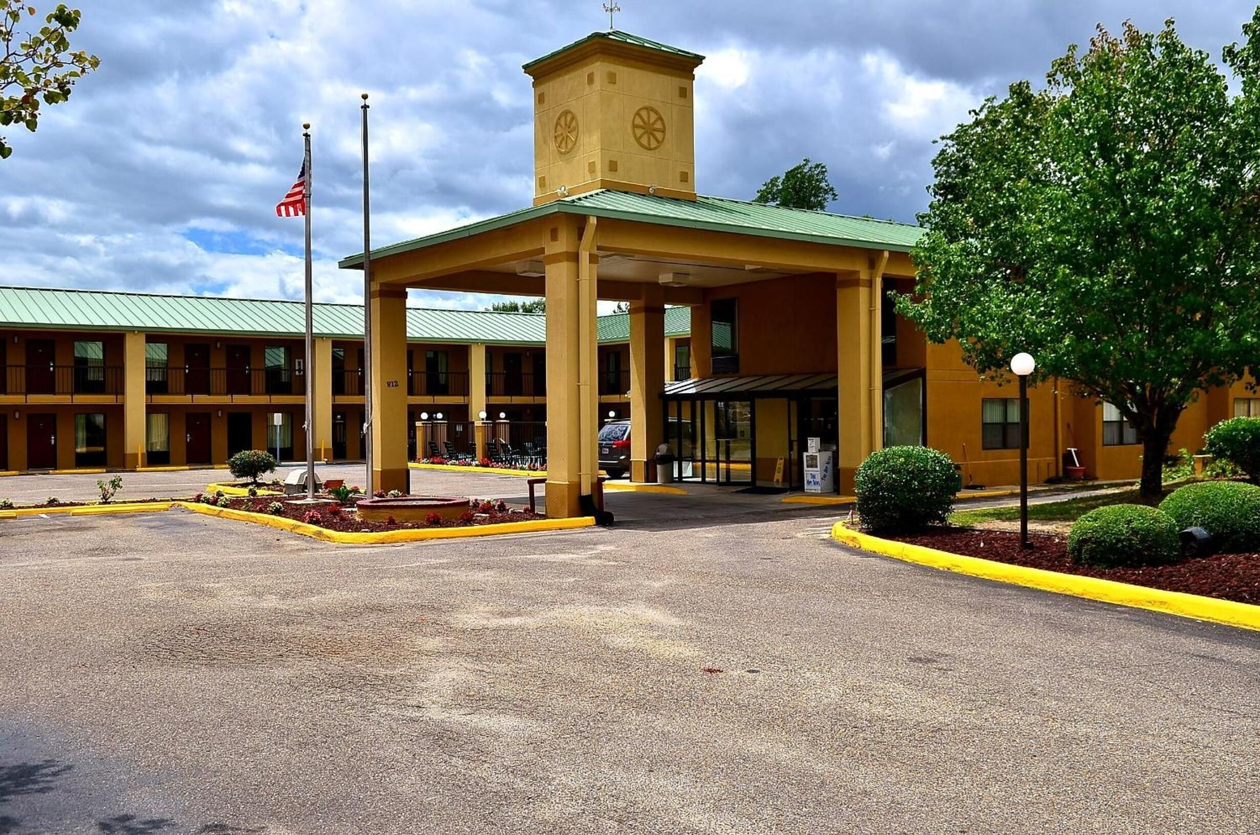 Un hotel con una torre centrale, un ingresso coperto e un parcheggio.