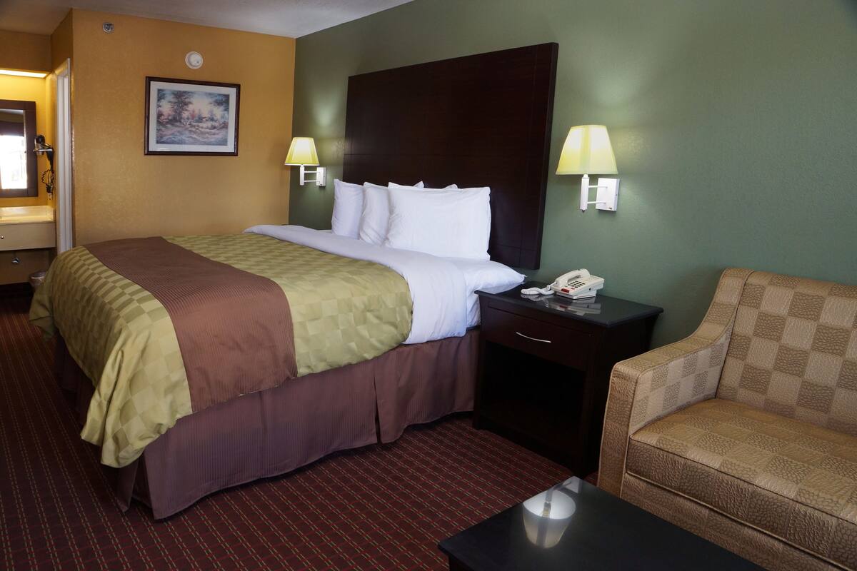 Una habitación de hotel con una cama grande, una mesita de noche con un teléfono, una silla y un cuadro en la pared.