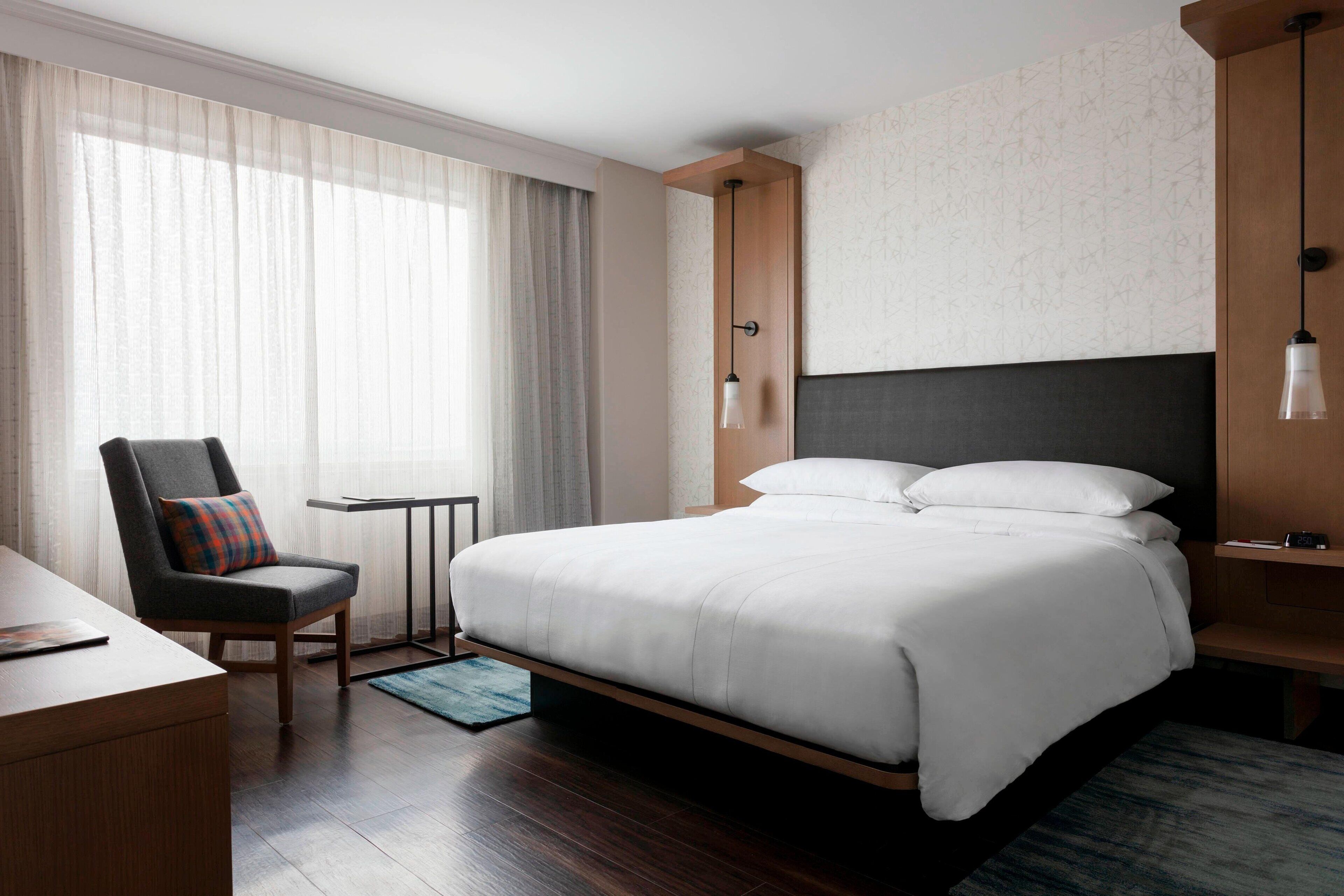 Habitació d'hotel moderna amb un llit gran, un escriptori, una cadira i una taula petita.