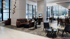 Eine geräumige Lobby mit großzügiger Sitzecke, einem gemusterten Teppich und großen Fenstern mit Blick auf die Stadt.