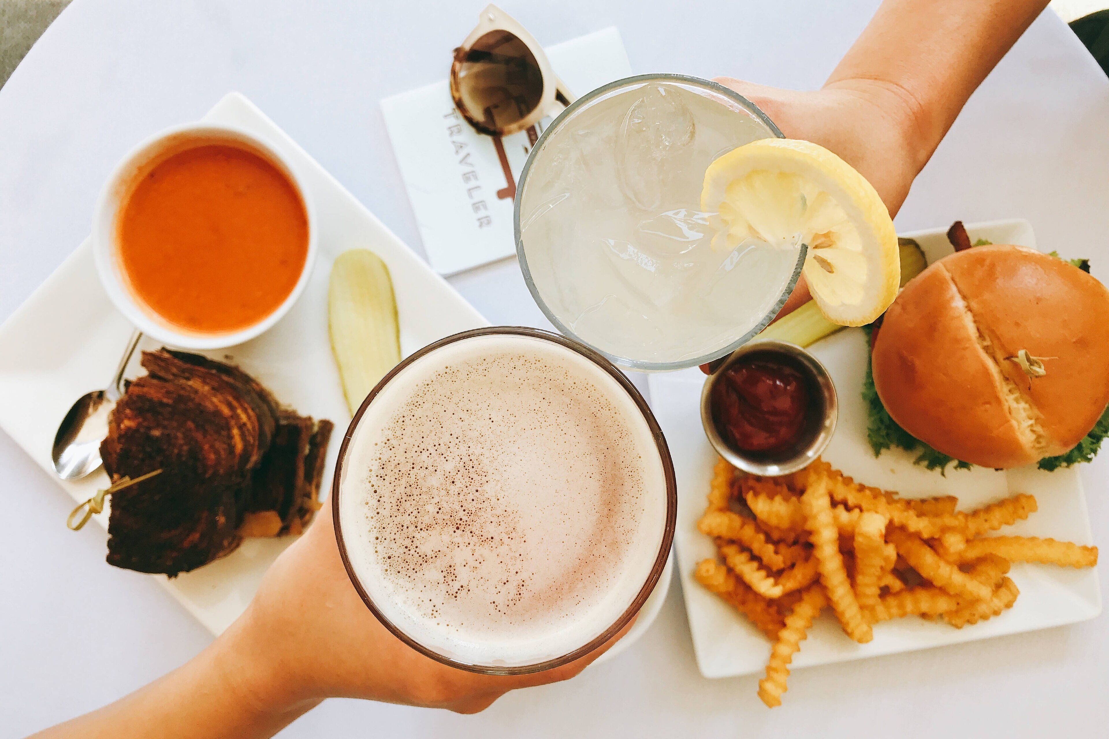 A table with a meal consisting of a burger, fries, a drink with a lemon slice, a bowl of soup, and a steak with a fork.