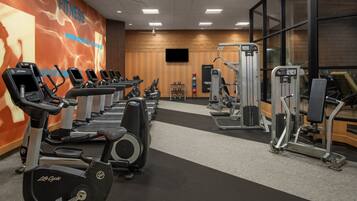 Une salle de sport équipée de nombreux appareils de cardio, de matériel de musculation et d’un grand écran de télévision fixé au mur.
