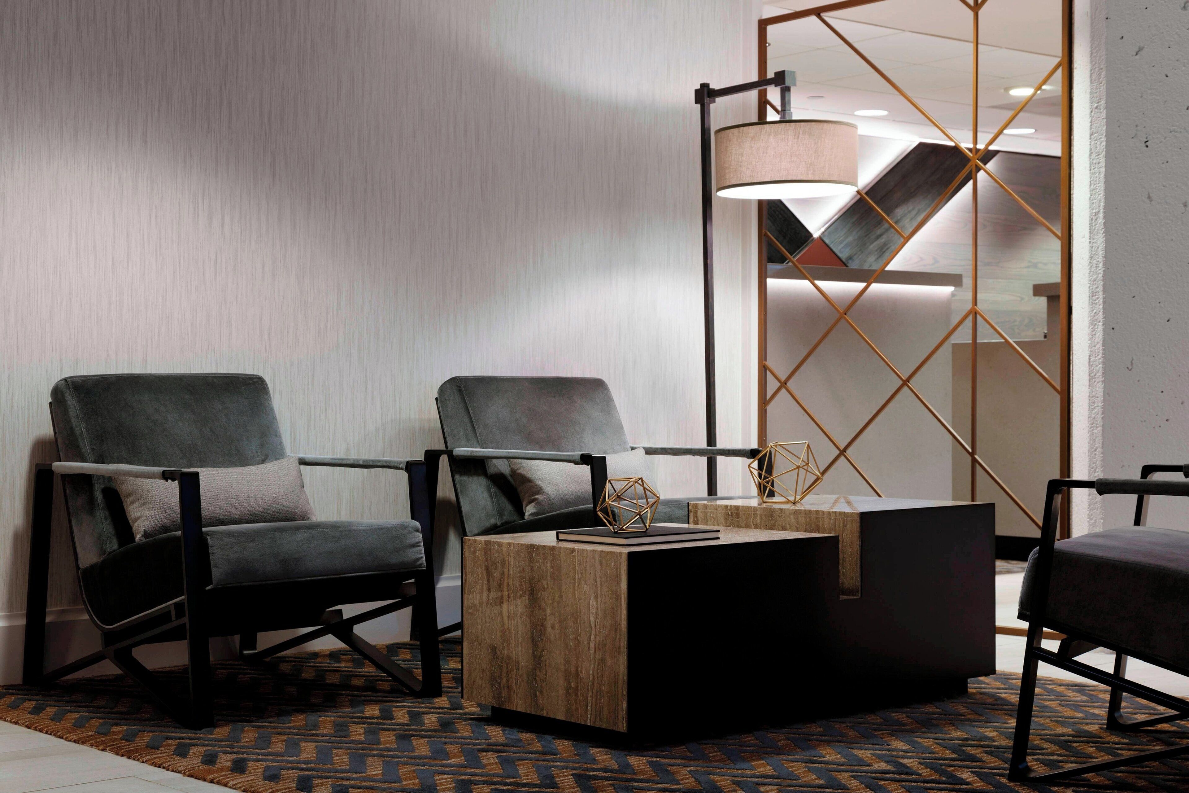 A modern room with two grey armchairs, a wooden coffee table, and a geometric-patterned rug.