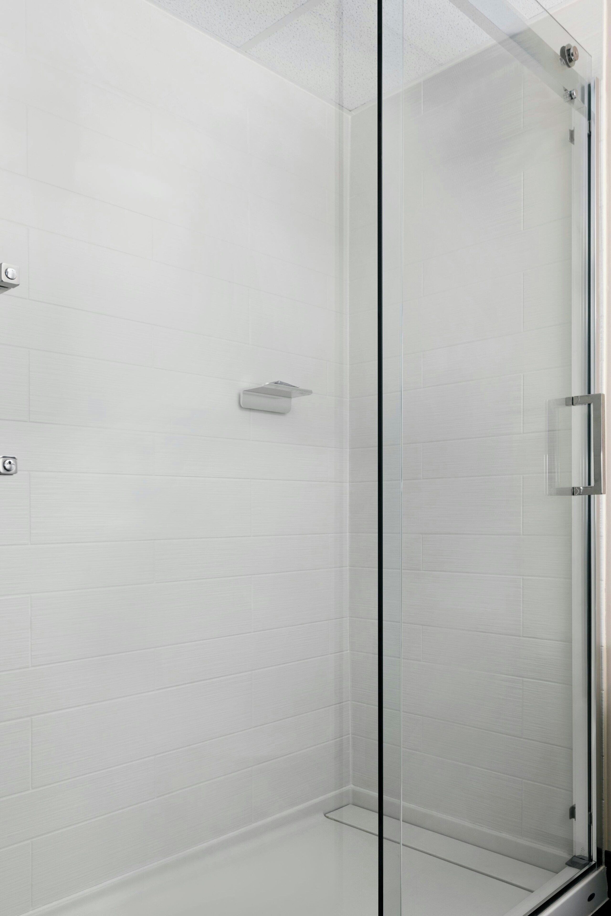 A glass-enclosed shower with white tiled walls and a metal handle.