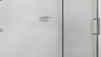 A glass-enclosed shower with white tiled walls and a metal handle.
