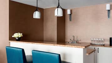 A kitchen with a granite countertop, two blue chairs, a vase with flowers, and pendant lights.