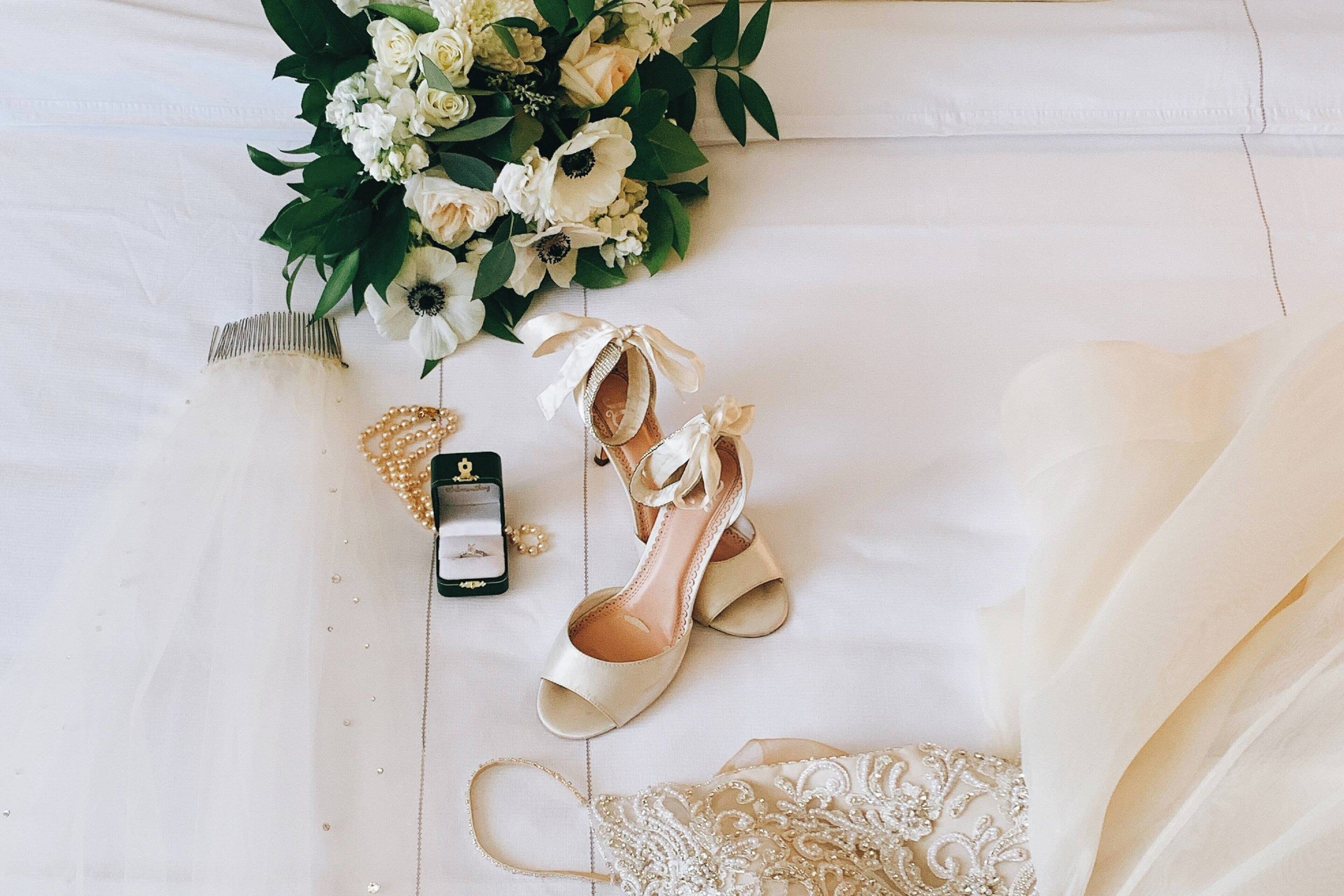 A wedding dress, a bouquet, a pair of shoes, and a jewelry box on a white surface.