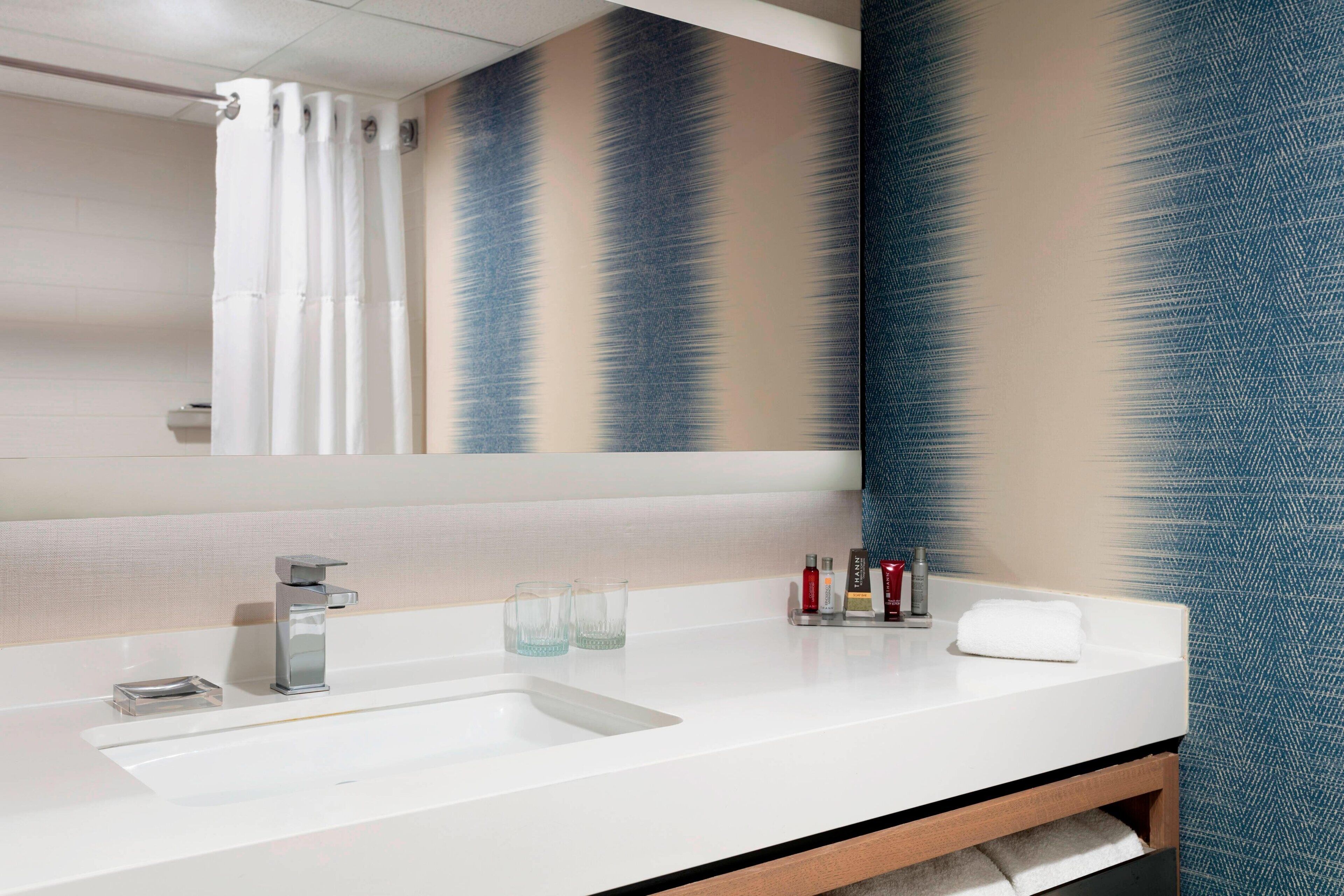 A modern bathroom with a white sink, a mirror, and a shower curtain.