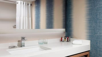 A modern bathroom with a white sink, a mirror, and a shower curtain.