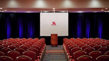 A conference room with rows of red chairs, a podium, and a large screen displaying the Marriott logo.