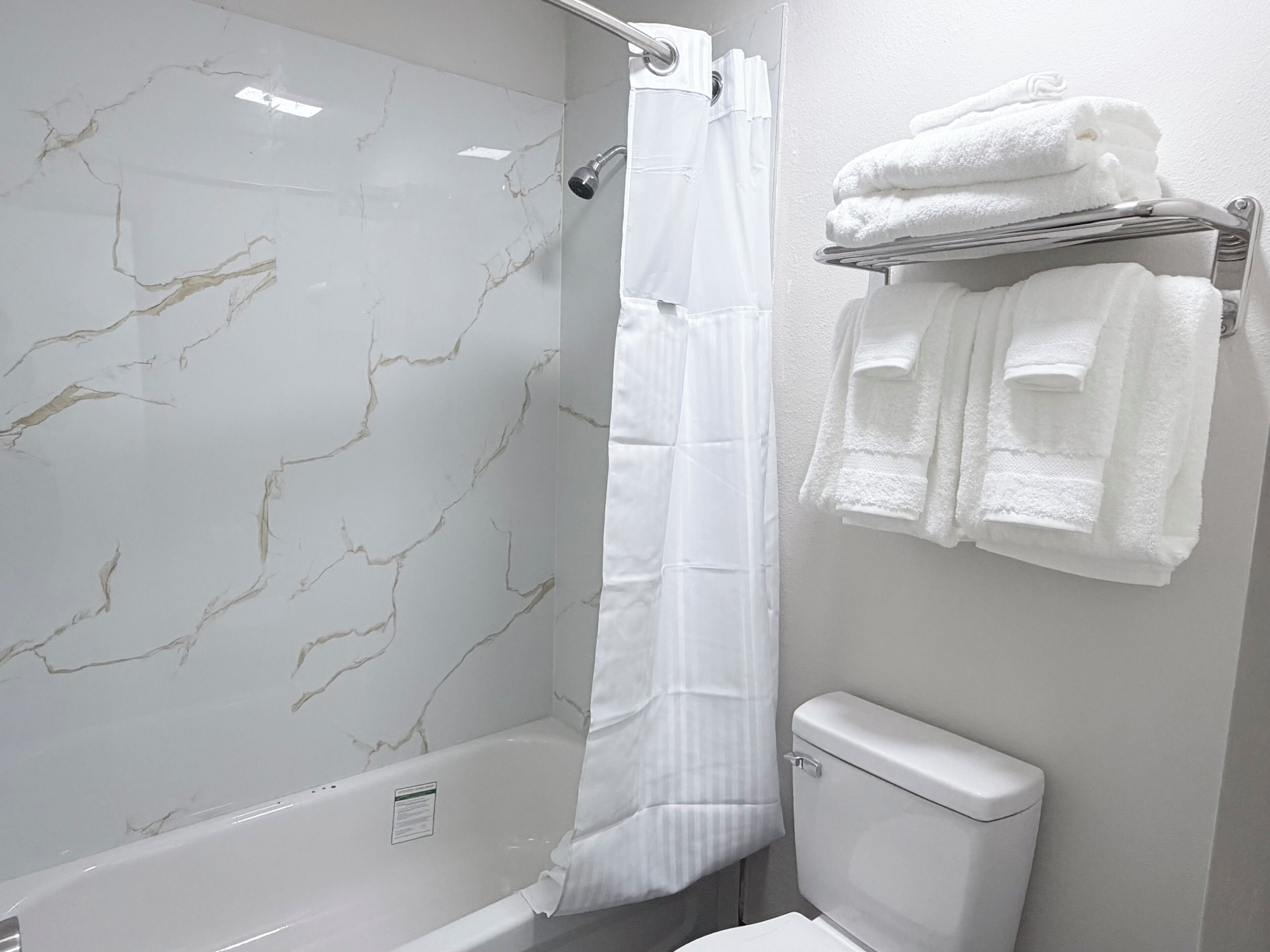 A bathroom with a marble shower wall, a white bathtub, and a toilet.