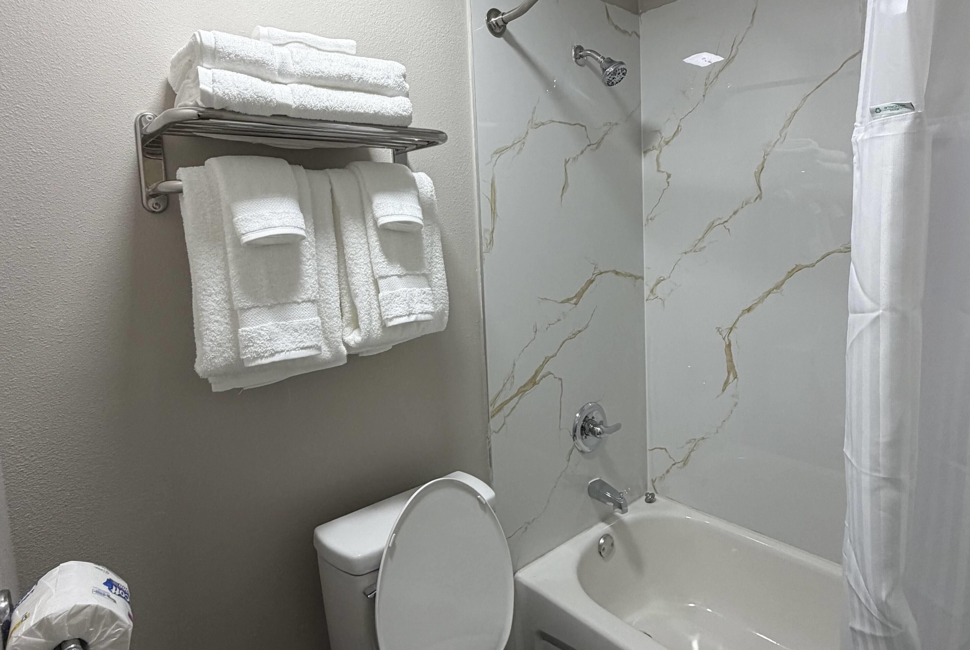 A bathroom with a toilet, a bathtub, and a towel rack with folded towels.