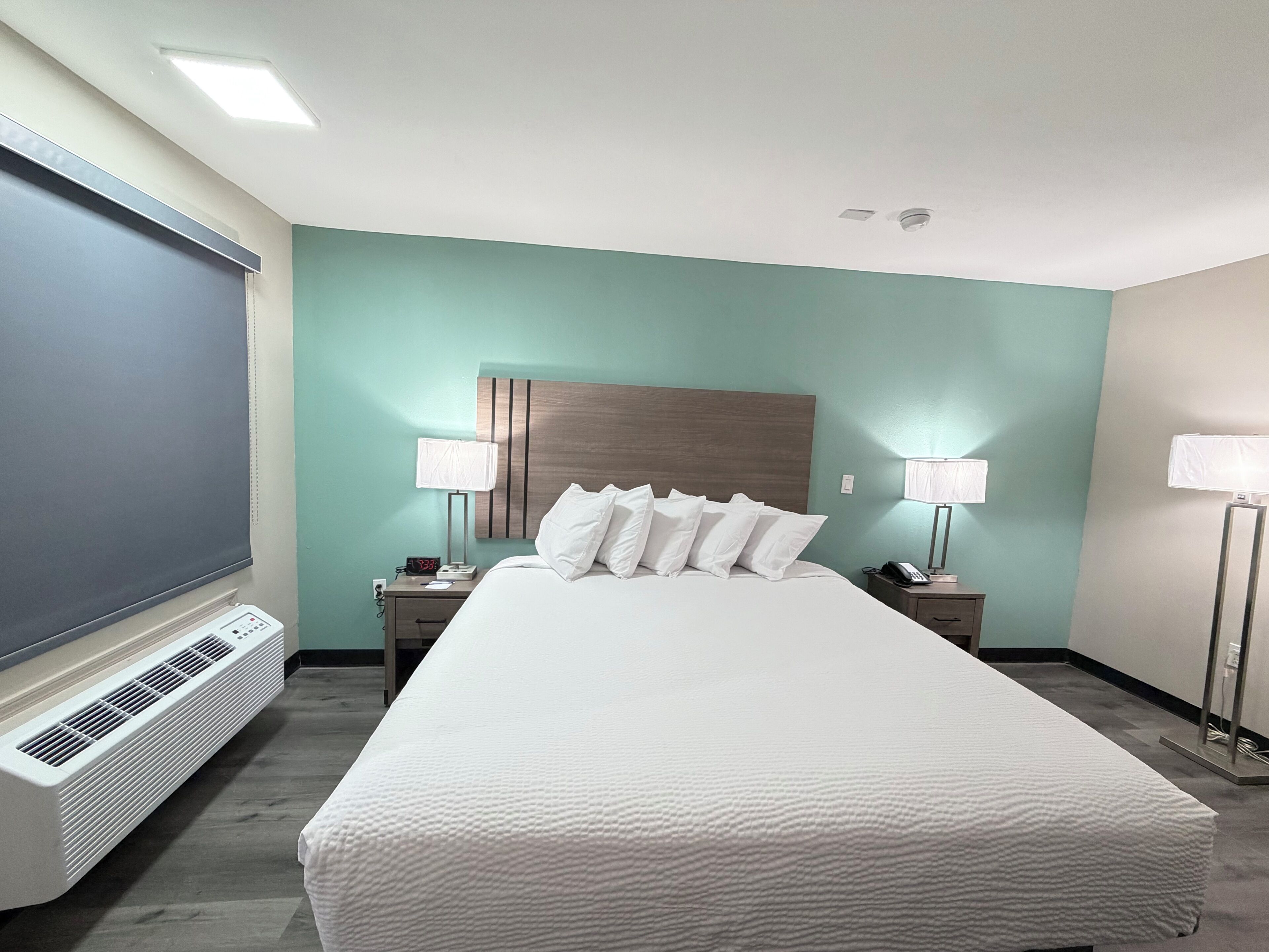 A hotel room with a large bed, two bedside tables, a TV, and a heater.