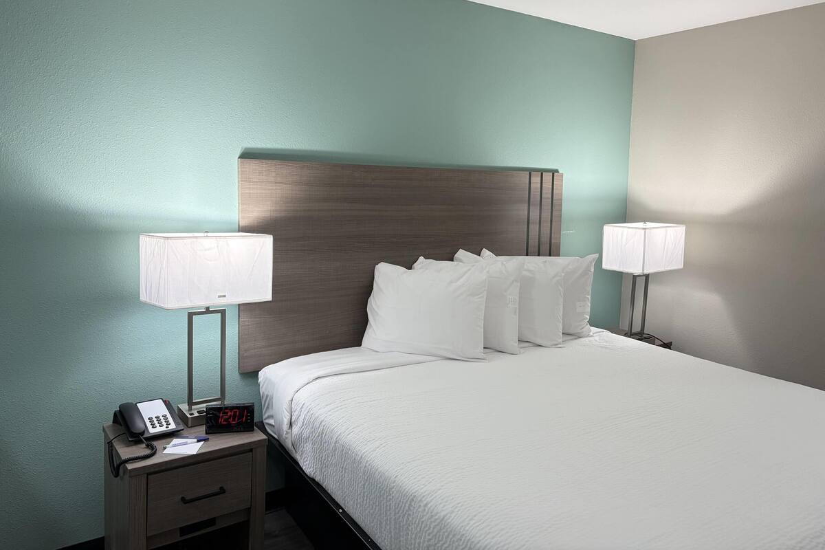 A hotel room with a bed, nightstands, lamps, a phone, and a digital clock.
