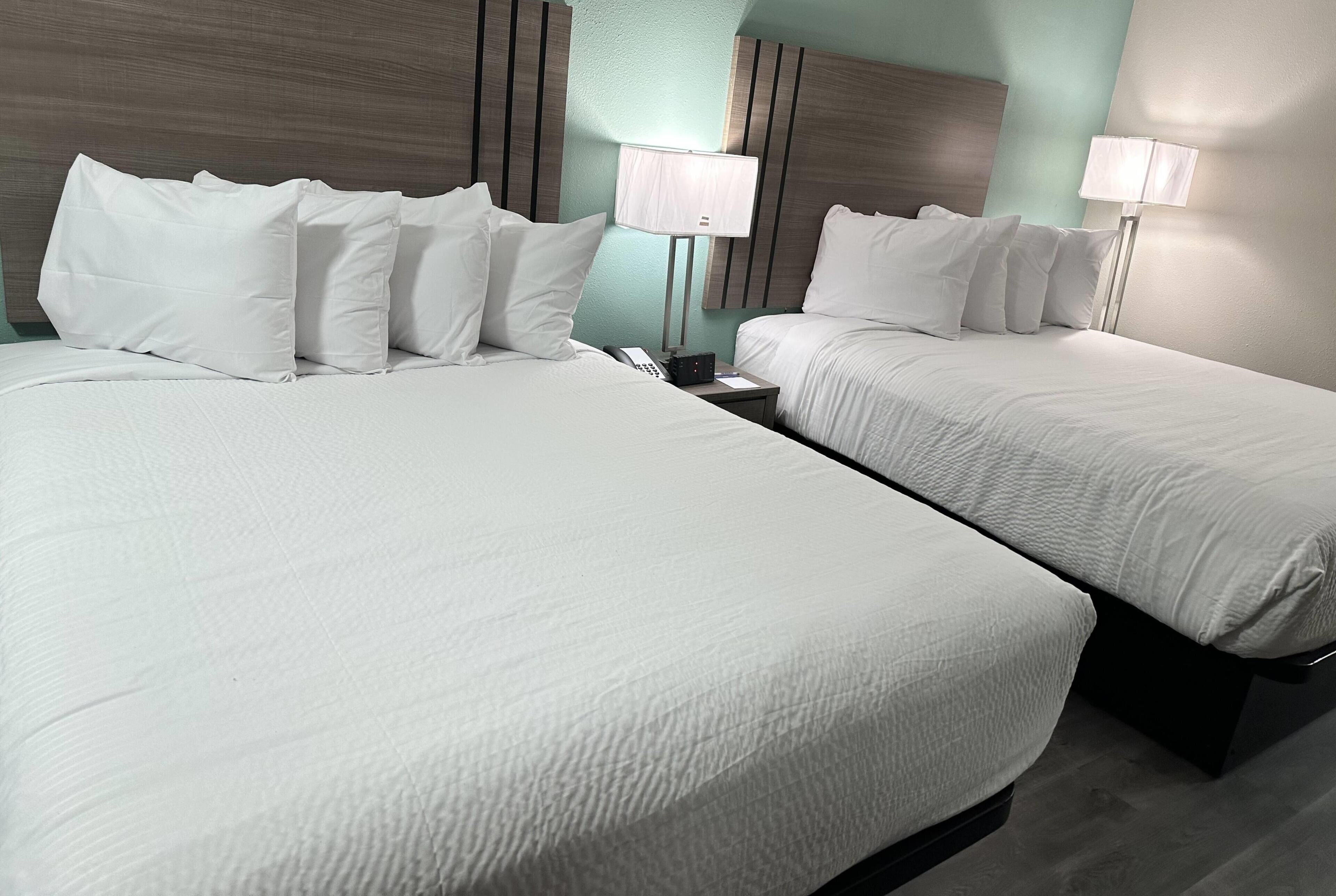 Une chambre d’hôtel avec deux lits, chacun doté de draps et d’oreillers blancs, une table de chevet avec une lampe et un téléphone.