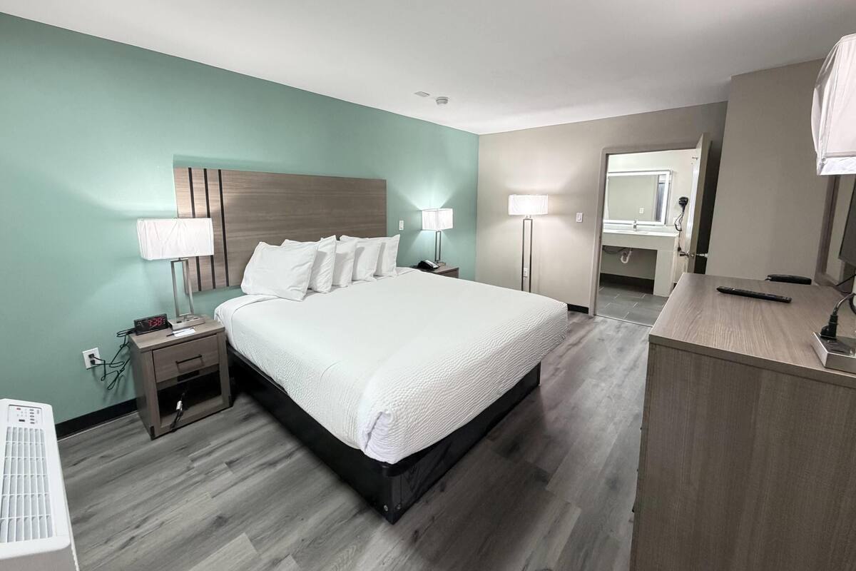 A hotel room with a bed, bedside tables, a desk, a lamp, a mirror, and a clock.