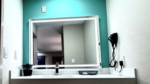A bathroom with a sink, mirror, hairdryer, and a teal wall.