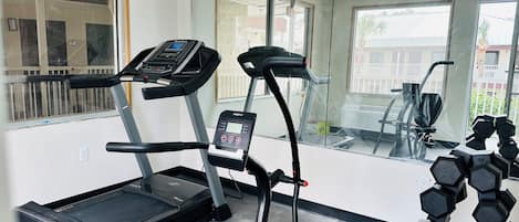 Un gimnasio con cintas de correr, una máquina elíptica y un juego de mancuernas.